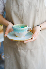 person in the apron holding handmade clay and turquoise cup of tea