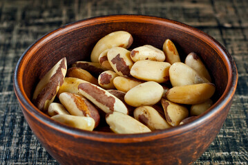 Brazil nuts in a clay bowl on a wooden table. Nuts on a black shabby board.