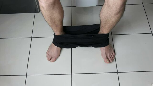 Legs of a man sitting on the toilet in the bathroom. Defecation process. Toilet at home. Healthy bowel movements in the morning.