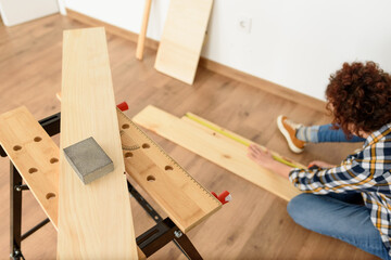 Close up shot of a wooden sandpaper on a workbench with a woman working in the background.