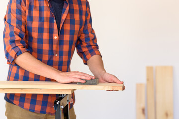Close up shot of a man at home sanding wood on a workbench.