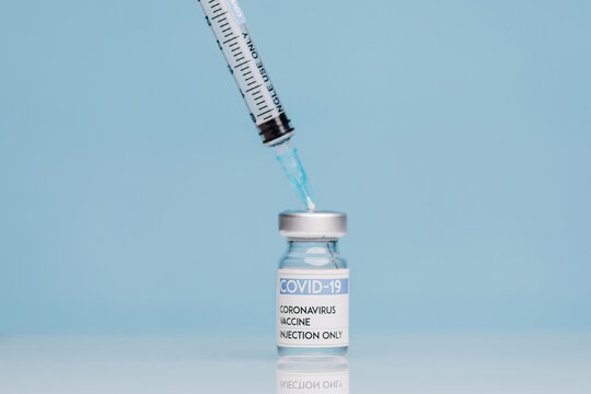 Medical syringe and glass vial with coronavirus vaccine placed against blue background