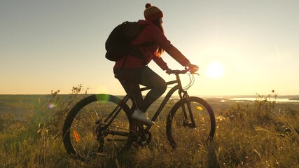 Naklejka na ściany i meble Woman of a cyclist traveler rides along the edge of the mountain, admiring the landscape and the sunrise. Free tourist rides a bike in nature in sun. Sports lifestyle. Cyclist exercising
