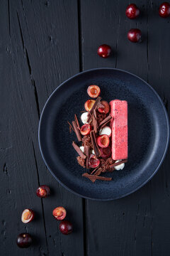Top view of yummy berry mousse pie served on black plate with cherries and chocolate flakes and placed on wooden table