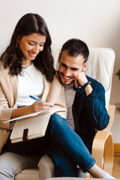 Content couple of musicians sitting together in armchair and taking notes while composing music at home