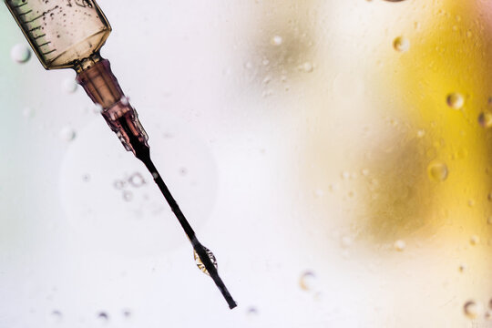 Closeup of needle of syringe filled with vaccine from virus injected in cell on blurred background