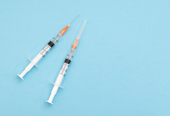 Two syringes with needles on a light blue background, with copy space