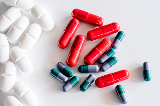 Top view of assorted colorful and white pills and capsules placed on white table