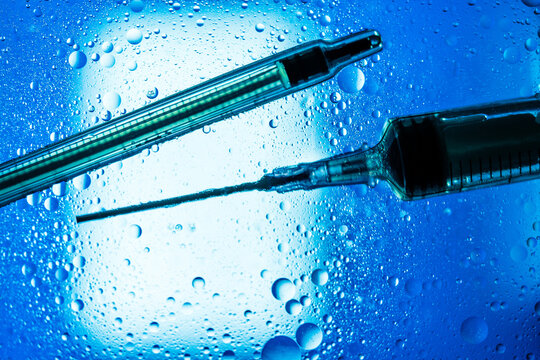 Closeup of syringes with vaccine placed on wet glass table with droplets illuminated by blue light