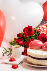mousse cake in white glaze with two big pink hearts, a cup of coffee and a bouquet of red roses
