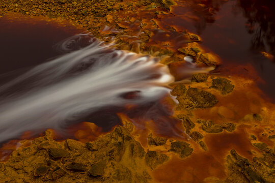 Magnificent scenery of river flowing in area with orange rocks in long exposure in Minas de Rio tinto