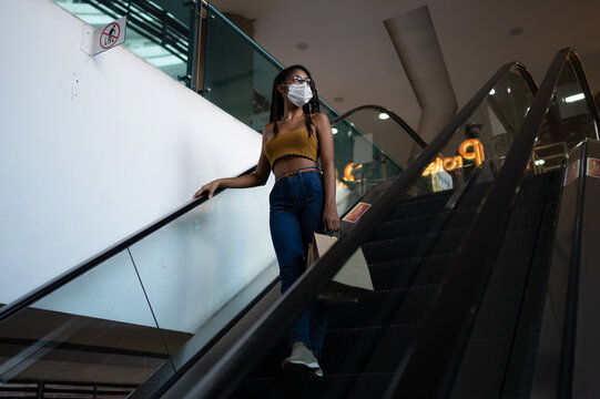 Contemplative young afro latin woman in a facemask uses escalator in a commercial mall, Colombia
