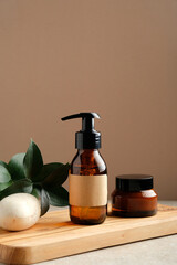 SPA natural organic cosmetics set on wooden board. Shower gel or shampoo amber glass dispenser bottle, jar of moisturizer cream, homemade soap, green leaf. Bath beauty product packaging design