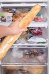 A person putting a loaf of wheat bread, baguette in reserve on a shelf of a home freezer, long life food storage concept