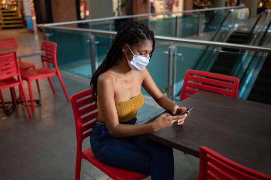 Portrait of attractive young afro latin woman wearing a facemask and using smartphone in a commercial mall, Colombia