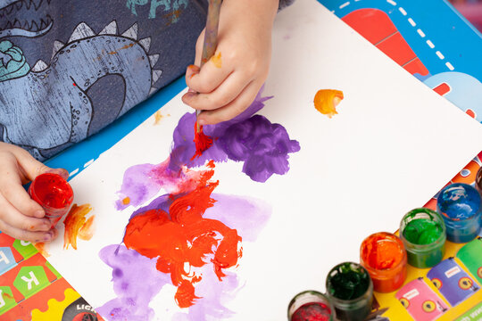 Kid hands start painting at the table with art supplies