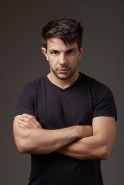 Man in black shirt with crossed arms looking at camera on gray background in studio