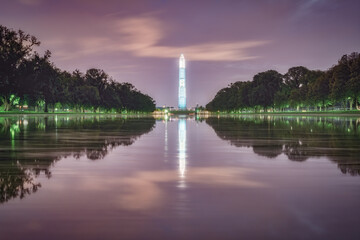 Obelisk Washington monument reflected in water surrounded by beautiful green park during the evening