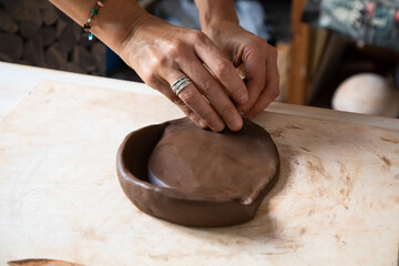 From above of crop anonymous male artisan rolling clay piece while creating plate in workshop