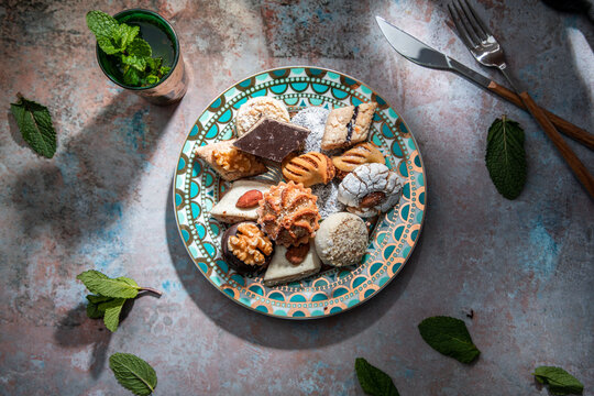 From above of baklava and biscuits with Moroccan peppermint tea near knife and fork placed on table decorated with mint leaves