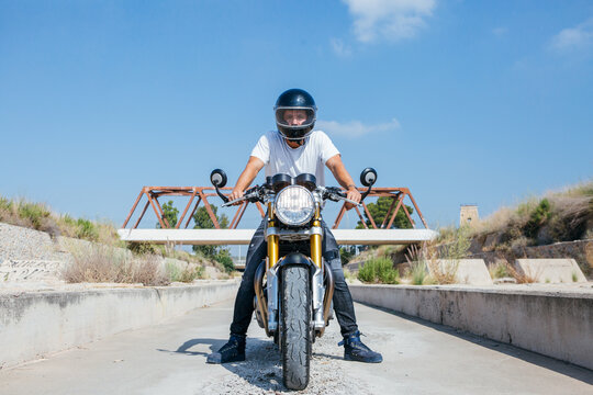 Confident male motorcyclist in protective helmet sitting on motorbike and looking at camera