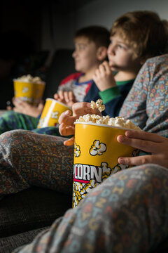Cropped young amazed siblings kids sitting comfortable on sofa with popcorn bucket while eating and watching TV