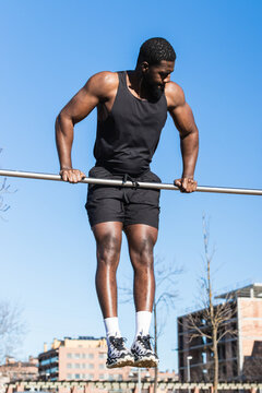 Handsome muscular African American male athlete pulling up on metal bar during training in city