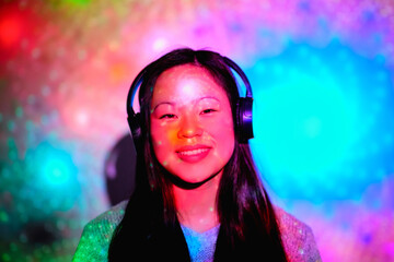 Stock photo of young asian woman listening to music in her room with colorful lights and looking at camera.