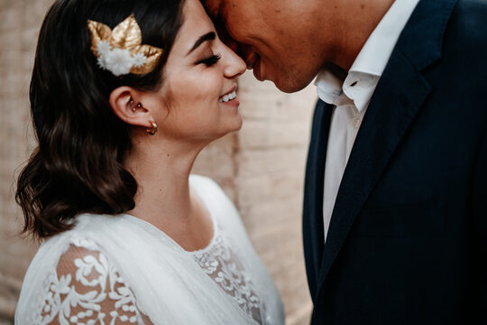 Side view romantic ethnic newlywed couple in elegant clothes bonding tenderly with eyes closed in light wedding studio