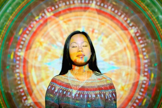 Stock photo of cool asian woman with a projection of a mandala in her face closing her eyes