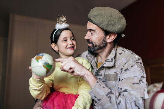 From below of positive soldier talking to daughter and pointing at place at globe before going to serve in army