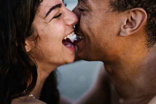 African American male traveler kissing sincere female partner standing against ocean during summer trip