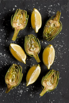 From above of halves of ripe green artichokes sprinkled with salt placed on black table in rows