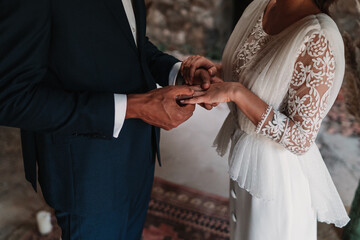 Side view of cropped unrecognizable ethnic groom putting ring on finger of bride in fancy wedding gowns holding hands gently with affection
