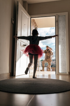 Low angle of surprised daughter running towards father returning from military service standing in doorway
