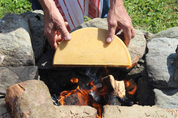 Raclette cheese is preparing in the fire . Traditional swiss melted cheese - raclette