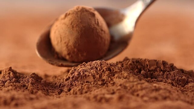 chocolate truffle is poured into cocoa powder with a spoon close - up slow motion