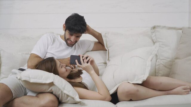A couple family. Happy middle east young man and Asian woman. People using a smartphone on social media internet and sitting on safa at home. Lifestyle in technology device. Multi ethnic