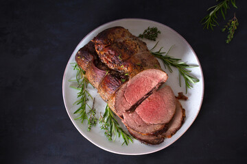 Sliced roast beef with herbs on plate. Overhead horizontal photo