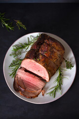 Sliced roast beef with herbs on plate. Overhead vertical photo