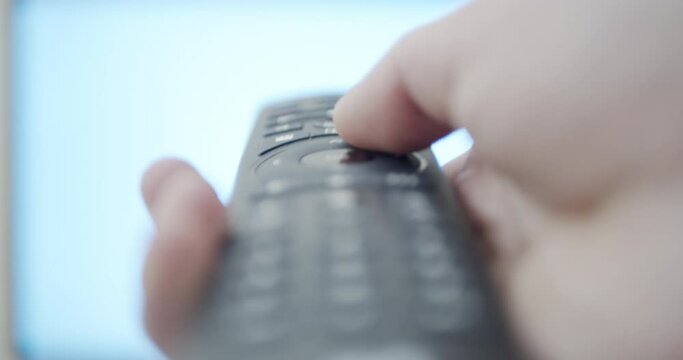 Controlling smart tv with remote control - close-up shallow depth of field footage with defocused screen in background