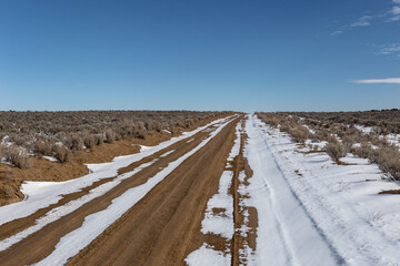 Long dirt road with snow cutting through open high desert in rural New Mexico on clear day