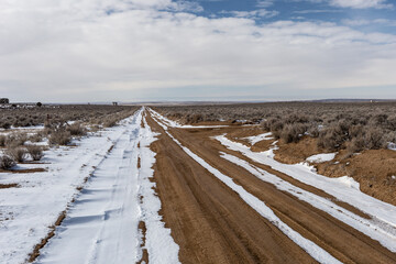 Snow along empty dirt road cutting through open high desert in rural New Mexico on clear day