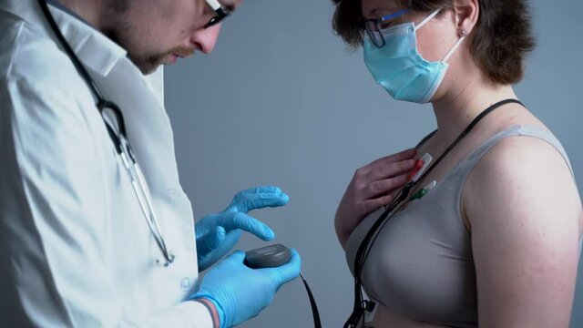 Young caucasian male doctor cardiologist do cardiological examination for woman patient with medical device holter monitoring ecg heart rate. Holter monitor test. Portable electrocardiogram. ECG