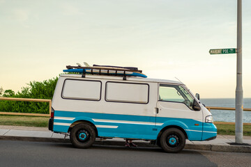 old surfing van with surfboards on a roof rack with beach and surf in the background.