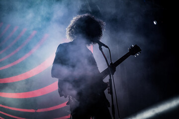 Obraz premium Guitarist stands silhouetted playing solo on stage with smoke, light beams and LED pattern 