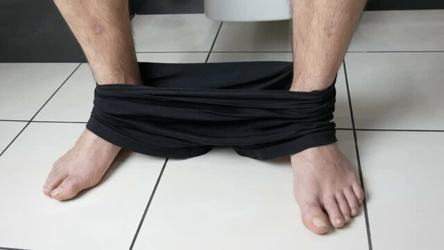Legs of a man sitting on the toilet in the bathroom. Defecation process. Toilet at home. Healthy bowel movements in the morning.