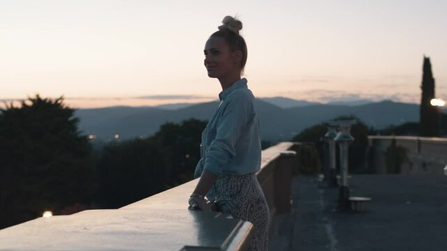 Blonde woman enjoying view over Florence in dawn, Orbiting shot of her leaning on a stone fense while looking in the distance. 4K 50fps, slow motion, smooth gimbal shot.