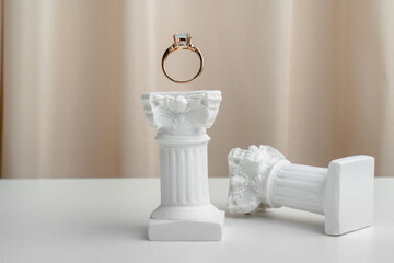 Gold ring stands on a white column against a beige background. Luxurious jewelry. Marry me. Wedding anniversary gift. Ring with diamonds