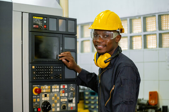 Engineering male african american workers wear soundproof headphones and yellow helmet working at operating CNC machine. work factory industrial concept.